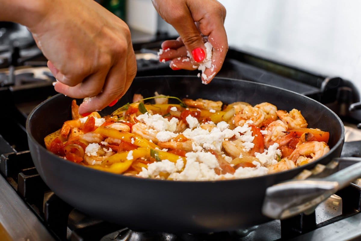 Crumbling feta cheese over the top of mediterranean sautéed shrimp.