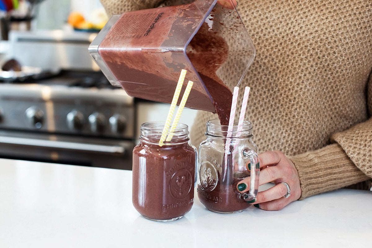 Pouring smoothie into mason jar glasses with straws in them.