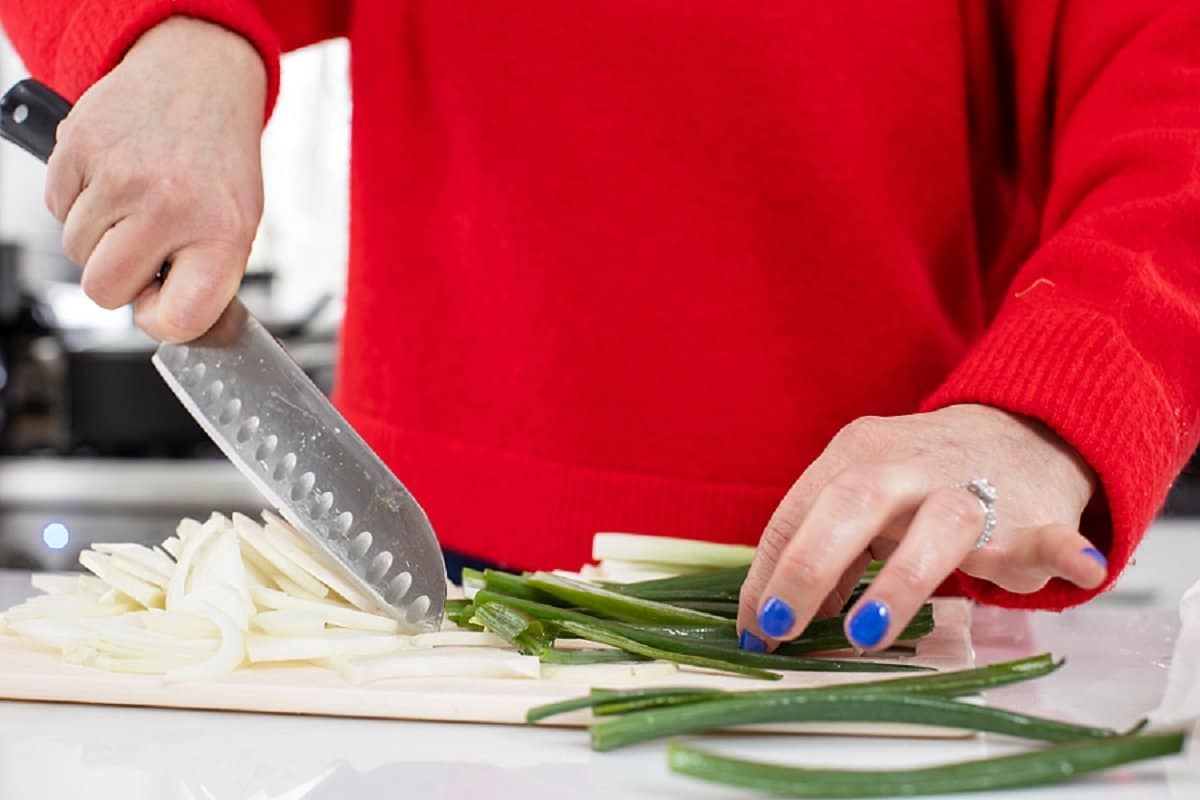 Liz cutting scallions with a sharp knife on a cutting board.
