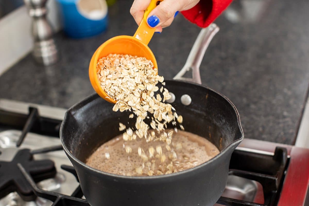 Adding oats to pot on stove.