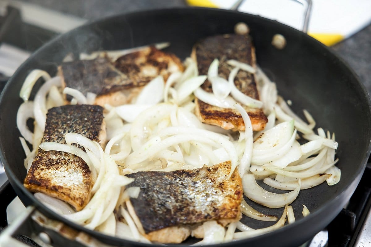 Cooking salmon fillets with sliced onions.