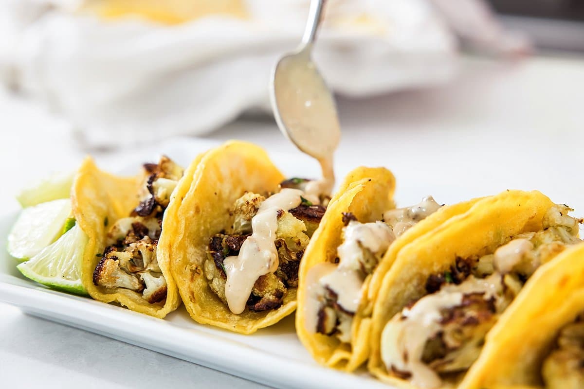 Drizzling chipotle tahini sauce on tacos