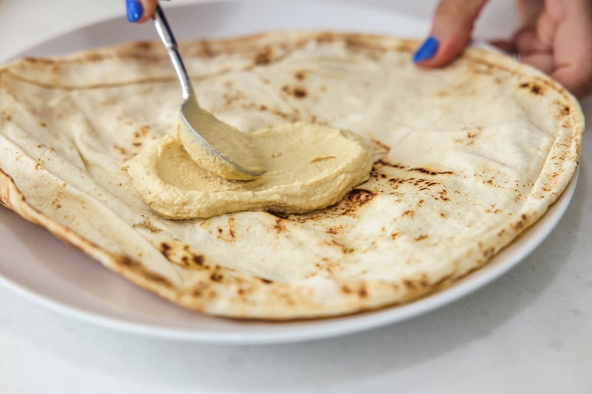 spreading hummus on pita bread