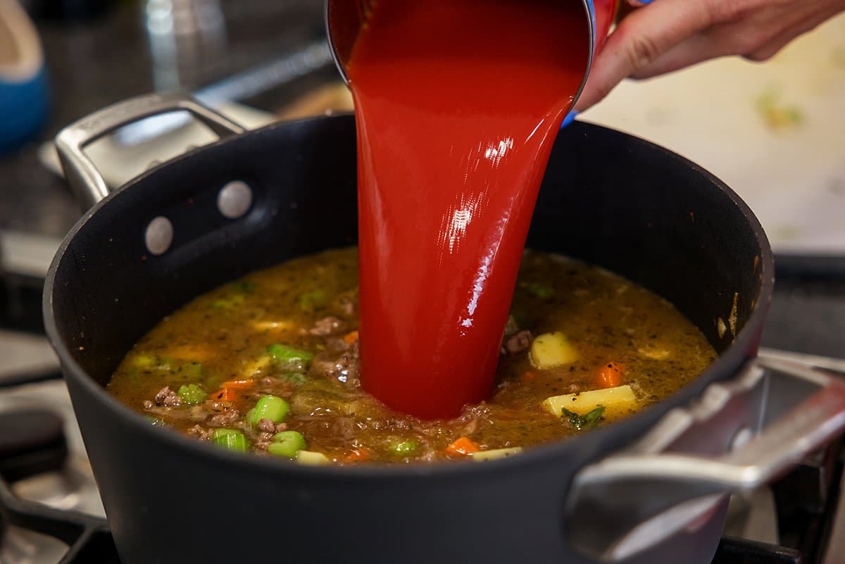 Adding tomato juice to soup in a pot