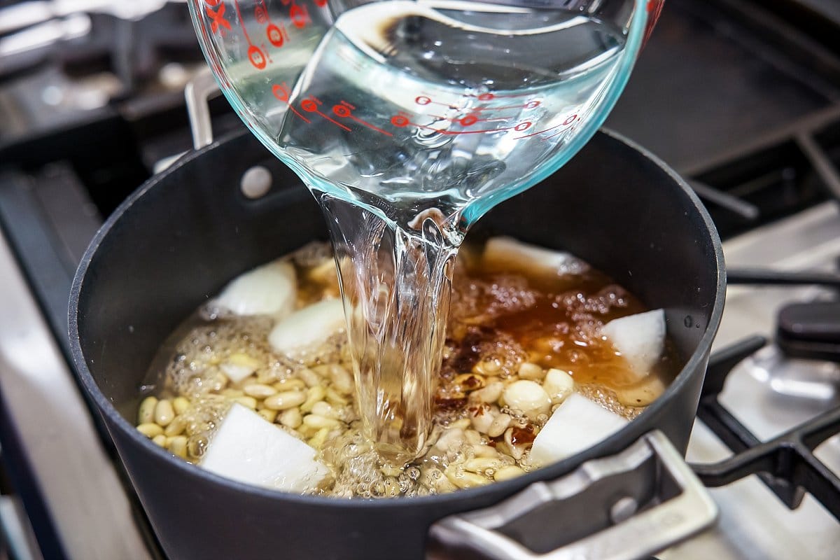 Adding water to pot of beans and aromatics.