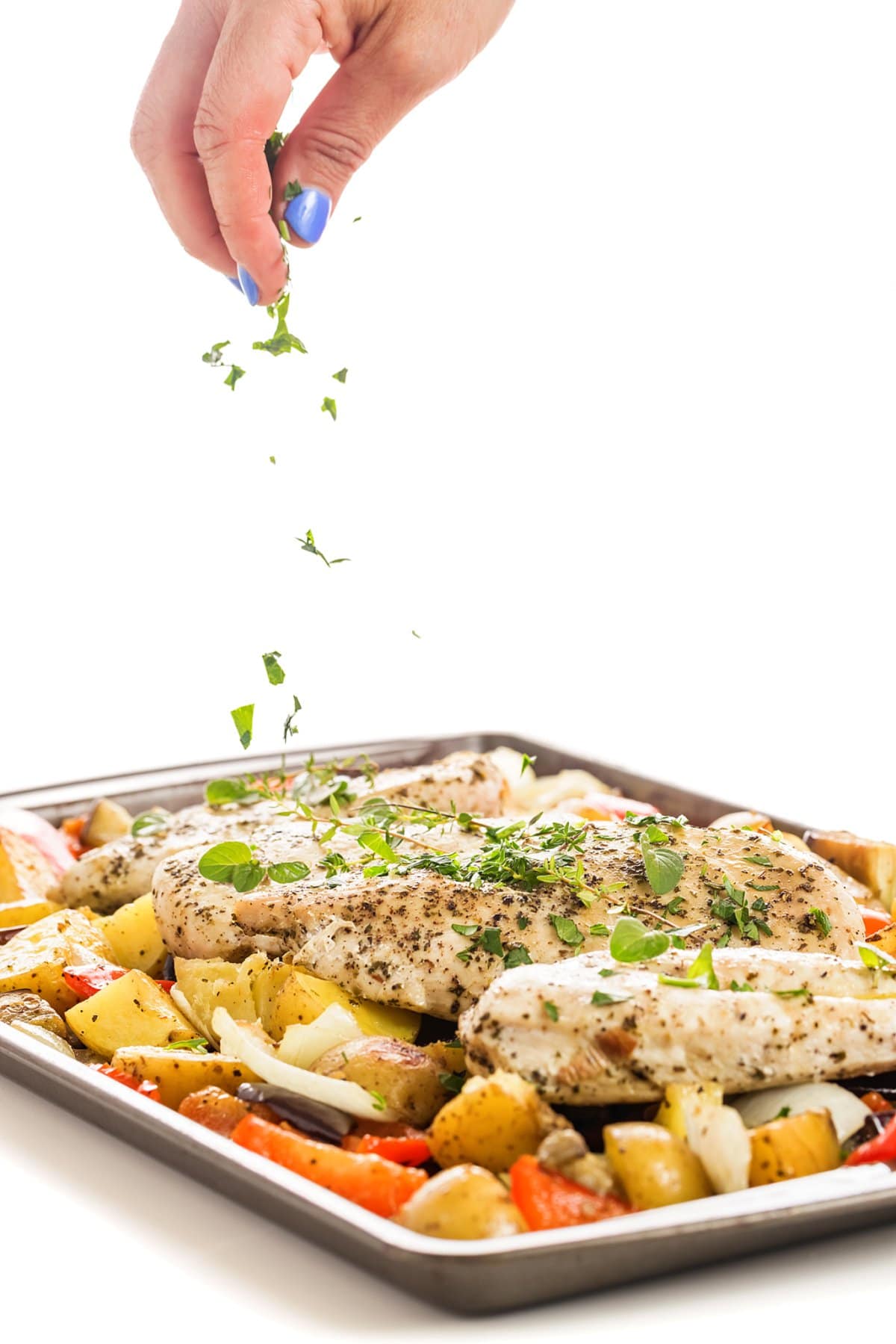 Sprinkling herbs onto sheet pan Greek chicken and vegetables.