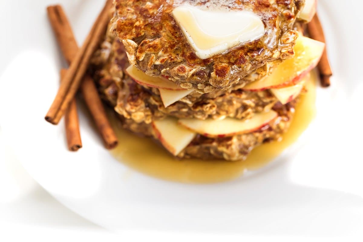 Apple cinnamon protein pancakes topped with butter and served with cinnamon sticks.