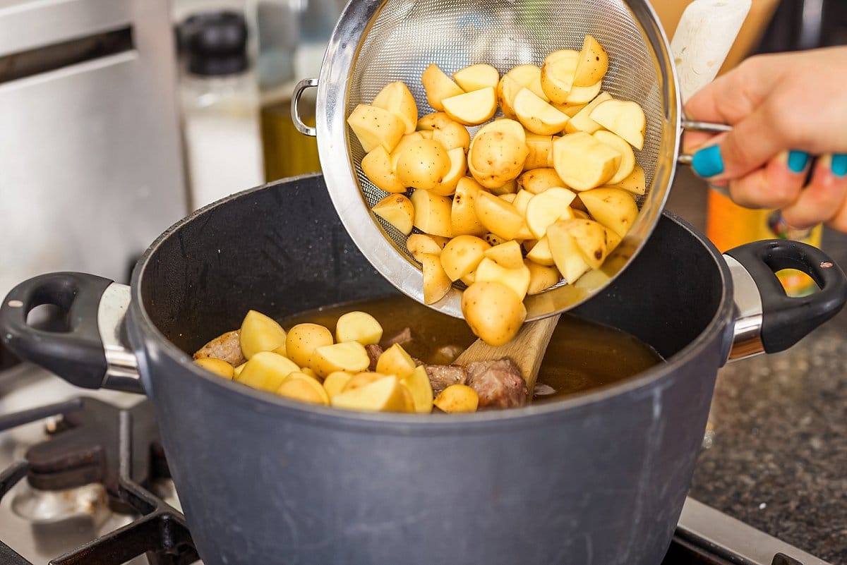 Adding chopped potatoes to a pot.