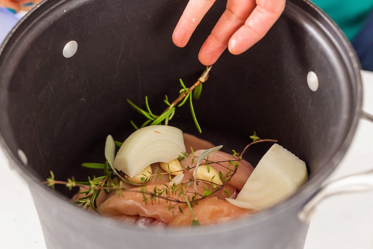 Adding onion and rosemary to the pot with chicken and garlic.