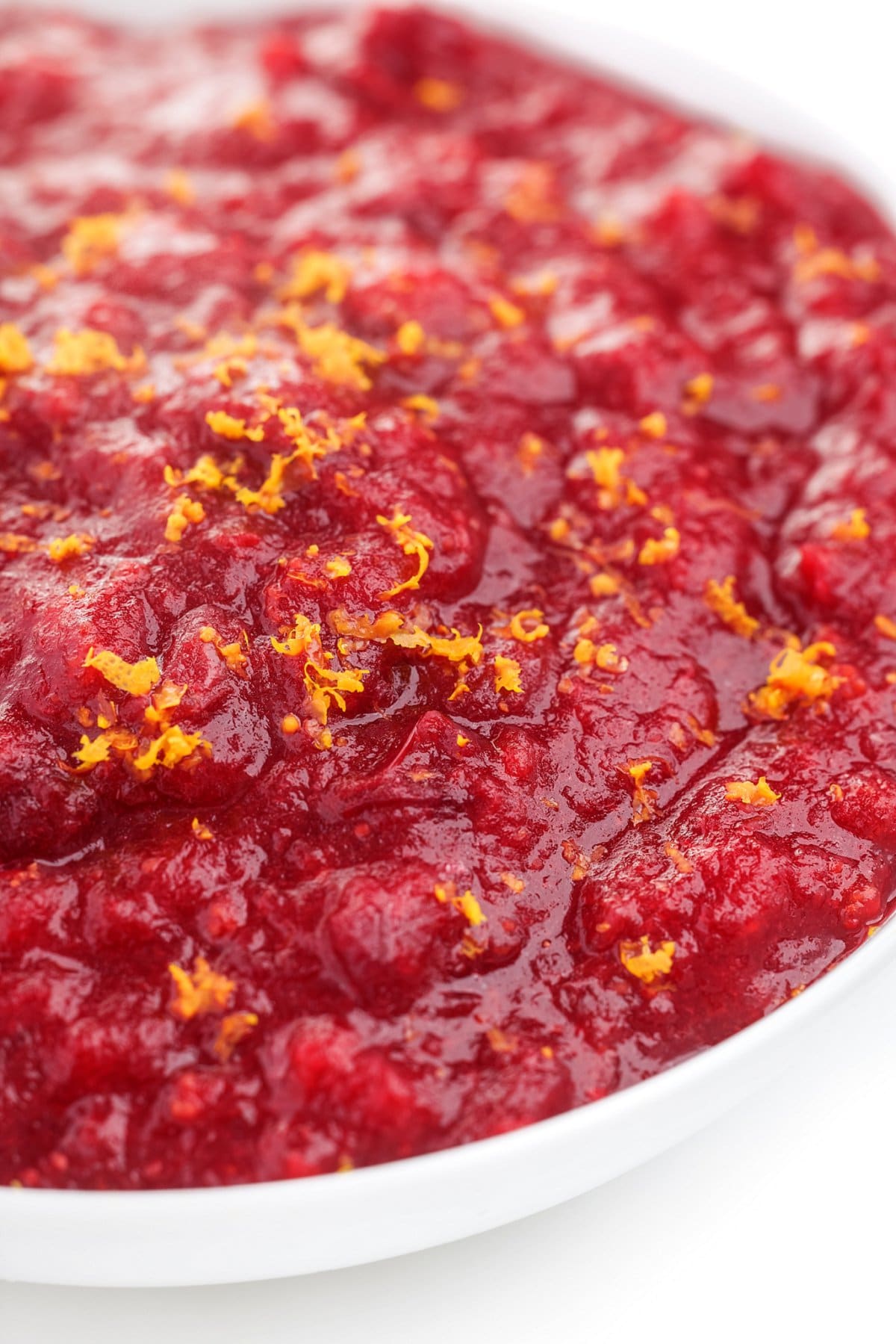 Slow cooker cranberry sauce with orange zest in a white bowl, a healthier Thanksgiving side dish.