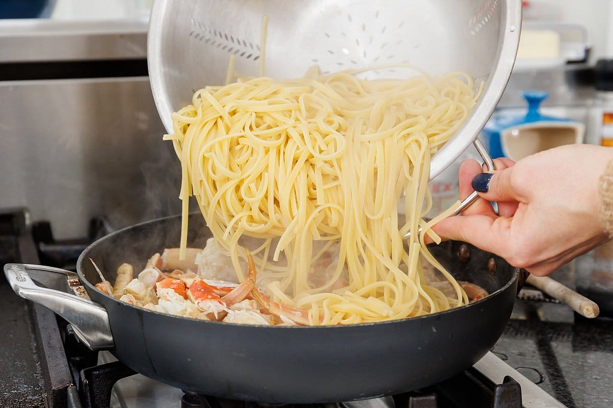 Adding cooked pasta to pan with crab legs.