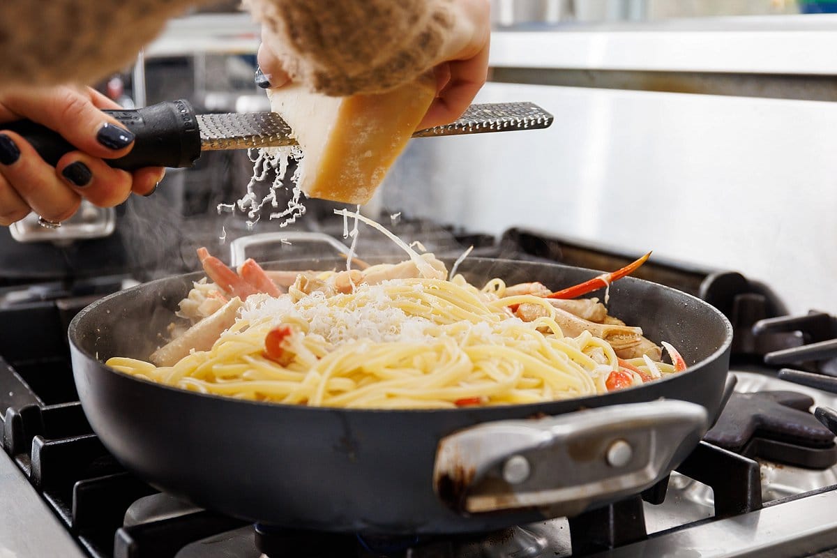 Freshly grating parmesan cheese over the top of crab linguine in pan.