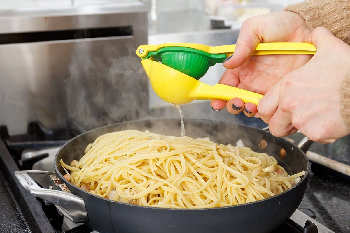 Using a handheld lemon juicer to juice lemon over pasta.