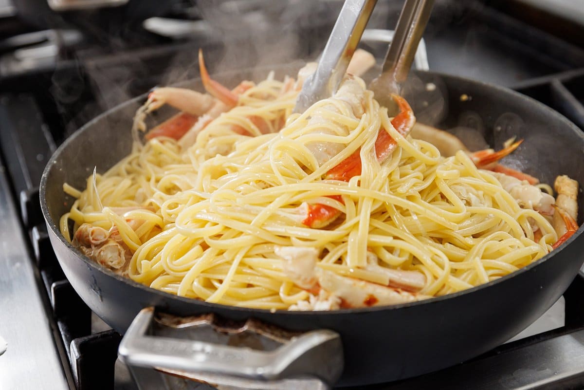 Using tongs to toss pasta and crab legs in white wine sauce.