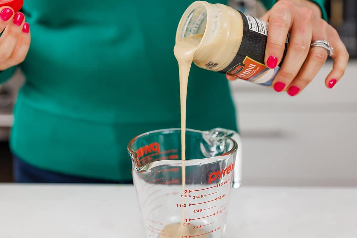 Pouring tahini into liquid measuring cup.