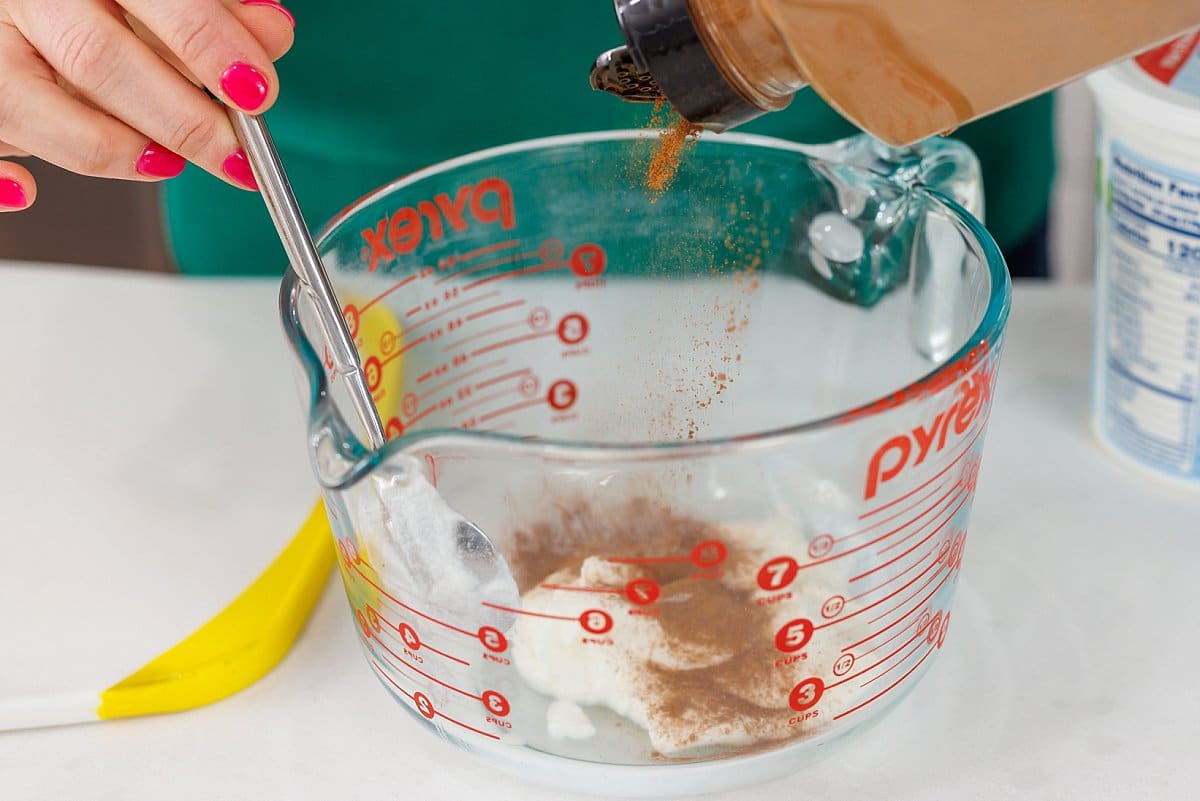 Adding cinnamon to yogurt in bowl.