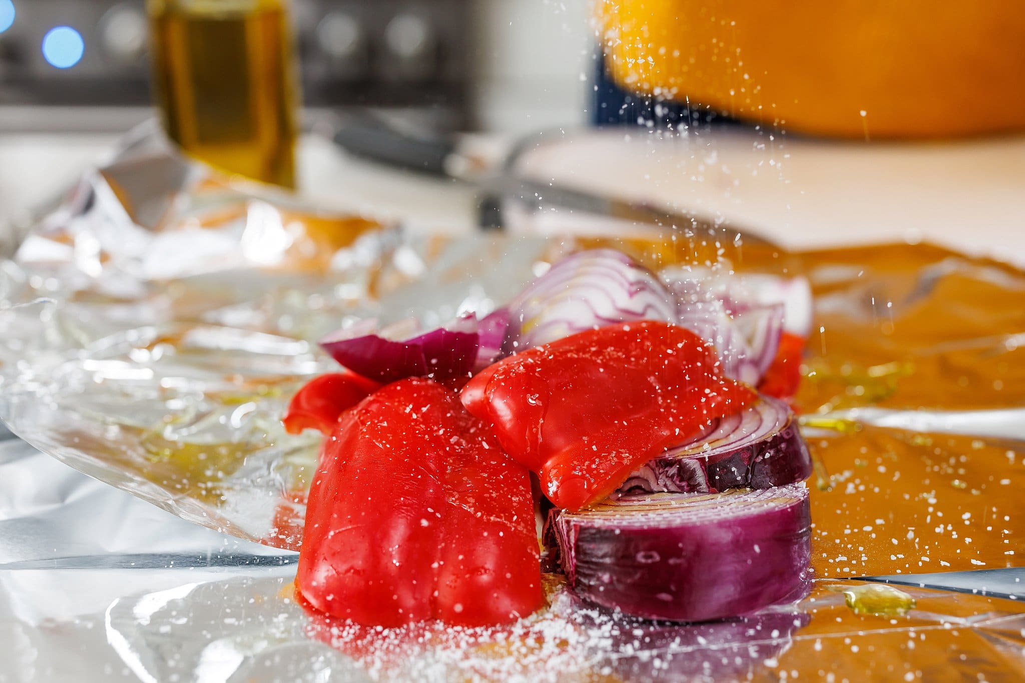 Seasoning red onion and red bell pepper with salt on top of tin foil.