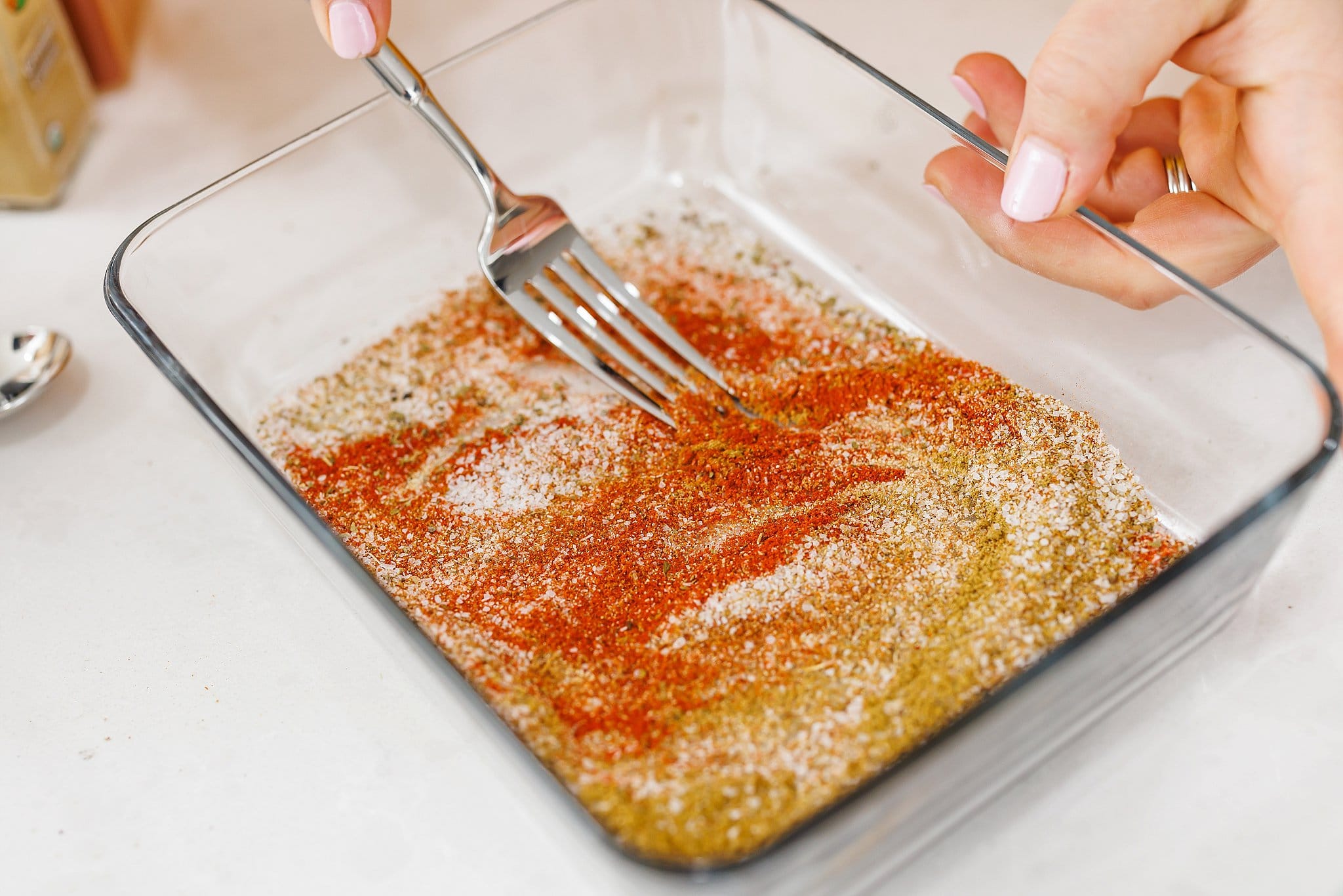 Using a fork to mix spices together in large glass dish.
