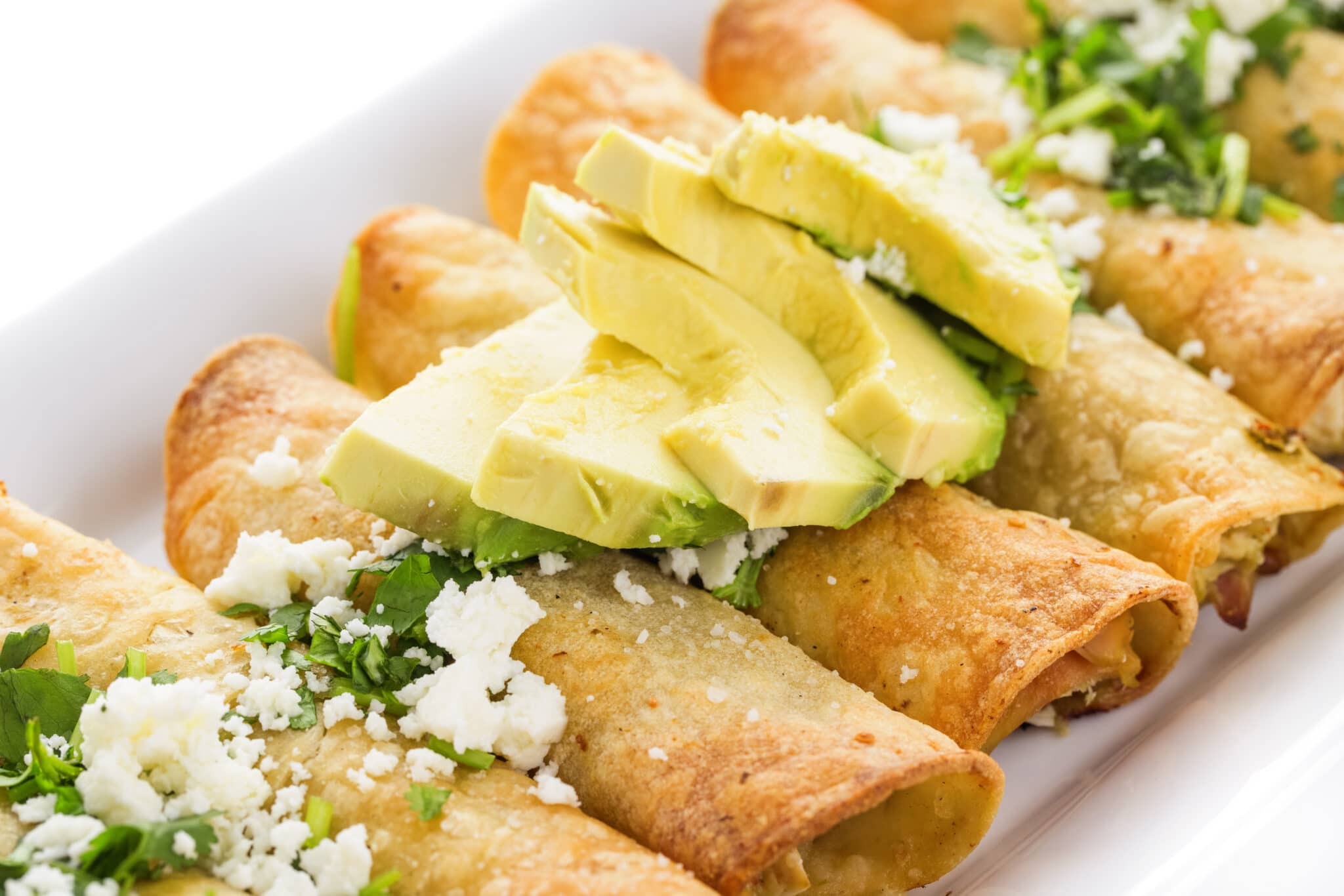 Baked taquitos topped with avocado slices.