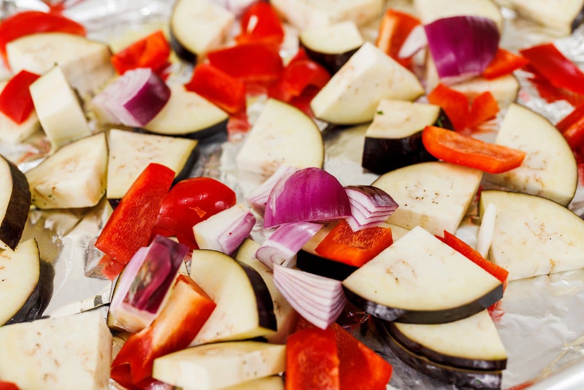 Eggplant, red onion, red pepper, and garlic cloves laid out on a sheet pan.