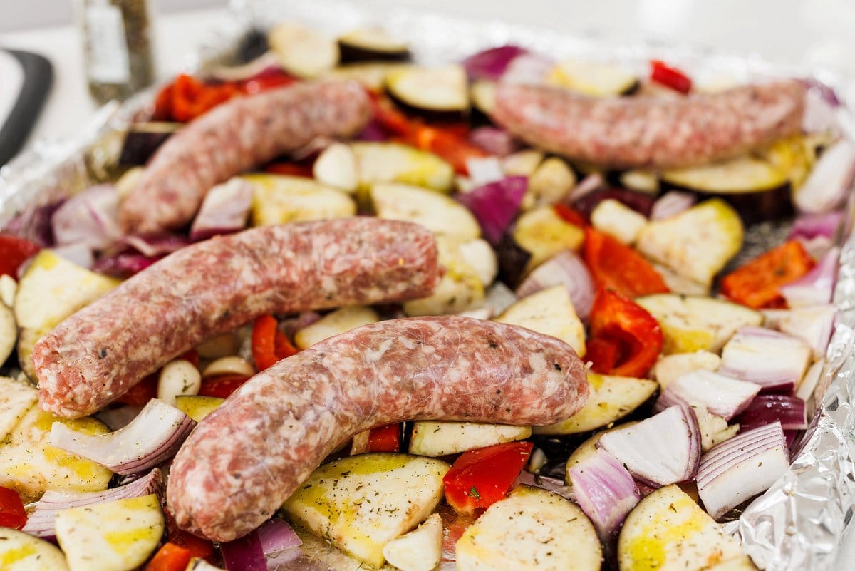 Laying sausage in casings on top of vegegtables.
