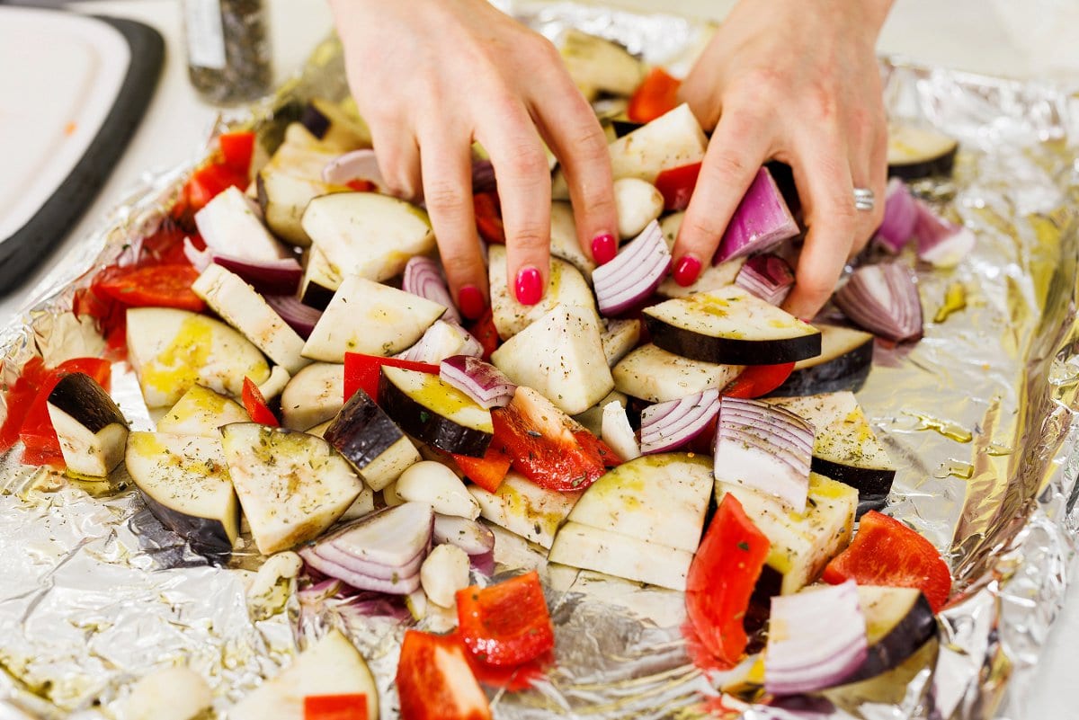 Tossing vegetables on sheet pan in oil and seasoning.