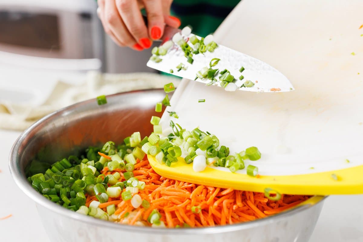 Adding pasta salad ingredients to large metal bowl.