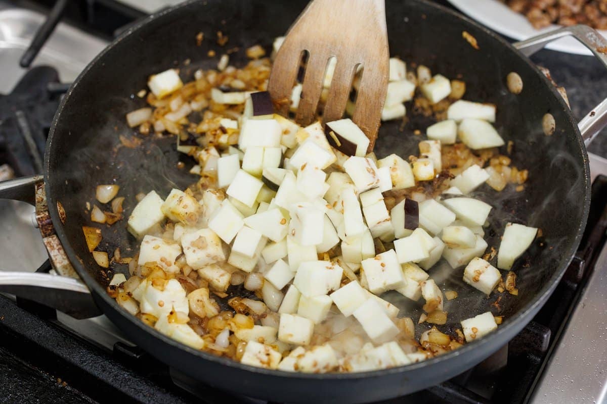 Adding cubed eggplant to skillet with cooked, diced onion.