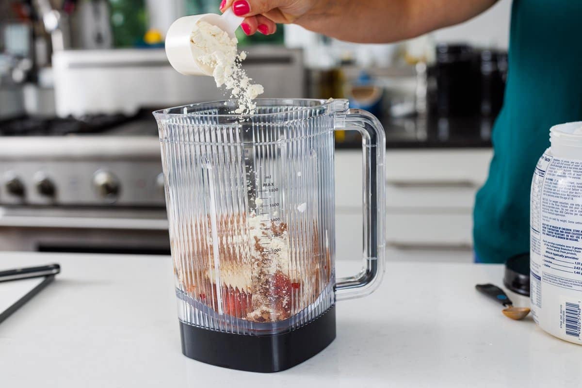 Adding protein powder to blender with fruit and yogurt.