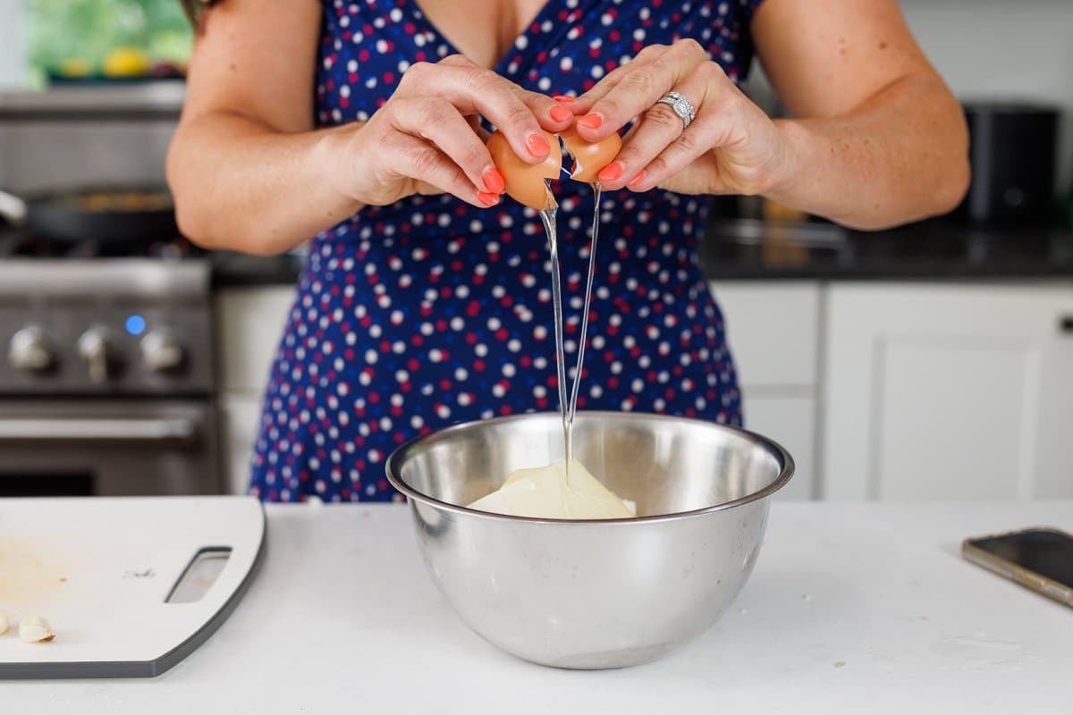 Liz cracking an egg into a large metal bowl with ricotta cheese.