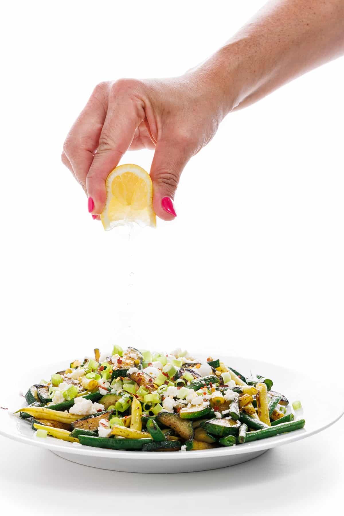 Garnishing zucchini and green bean sauté with fresh lemon juice.