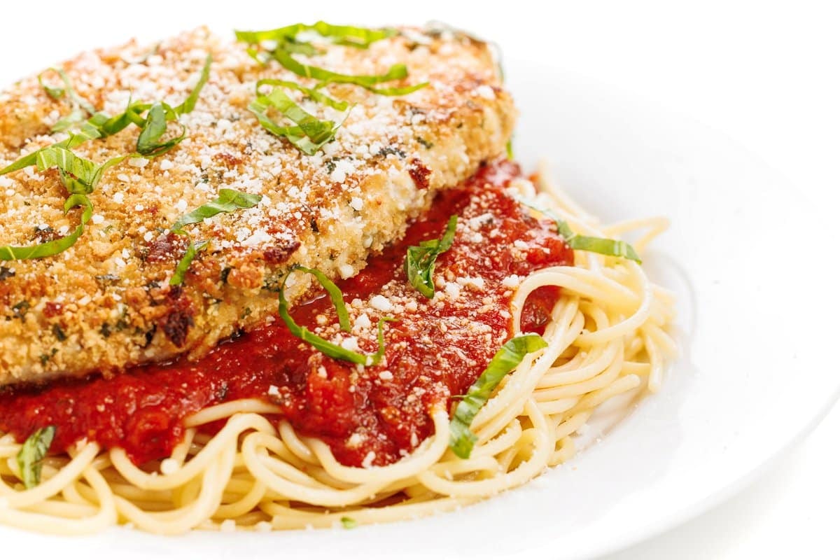 Oven baked chicken parmesan over pasta and garnished with fresh herbs.