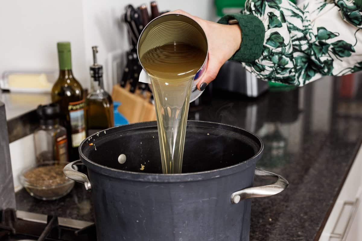 Pouring chicken broth into a large pot from a can.
