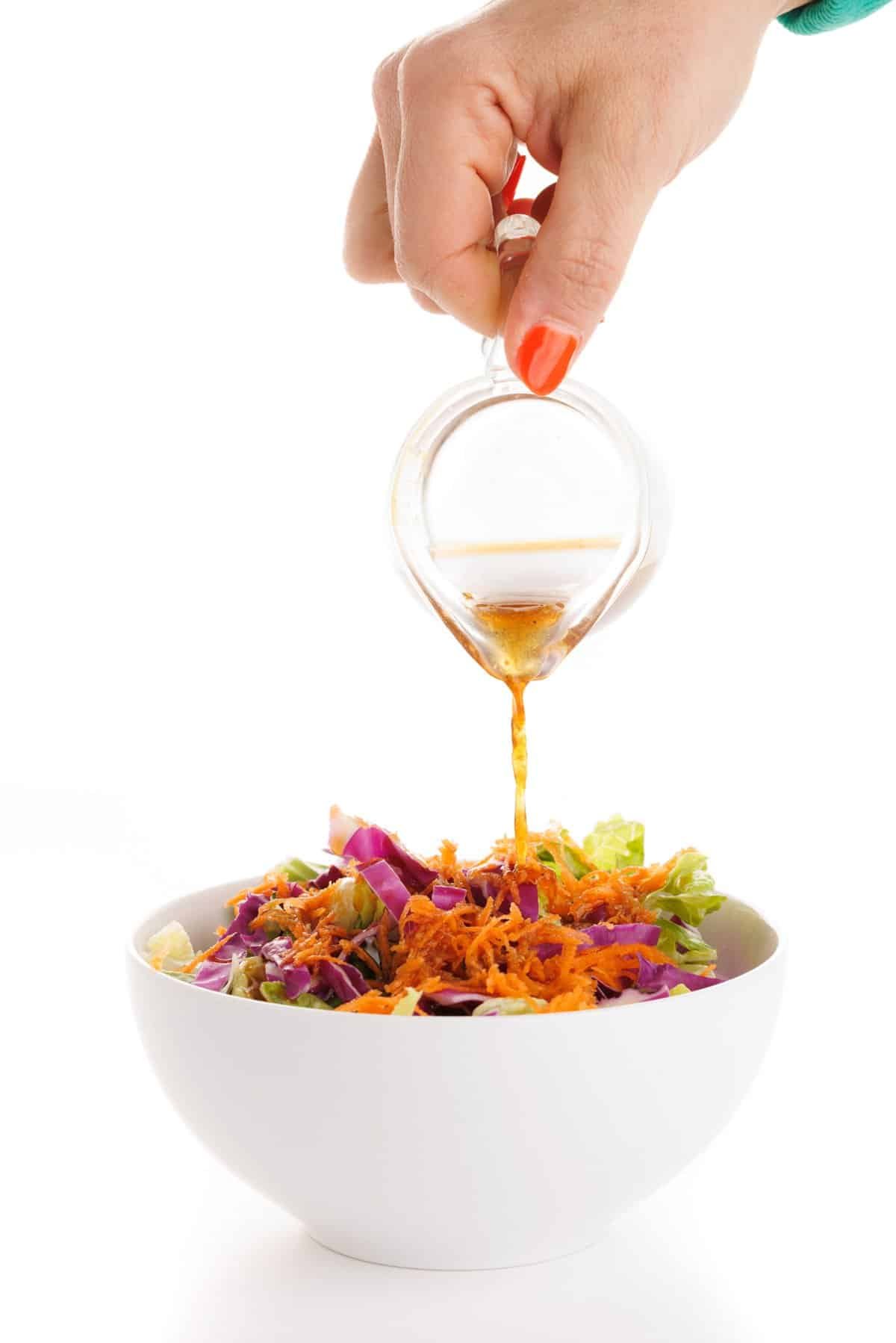 Pouring ginger salad dressing over greens.