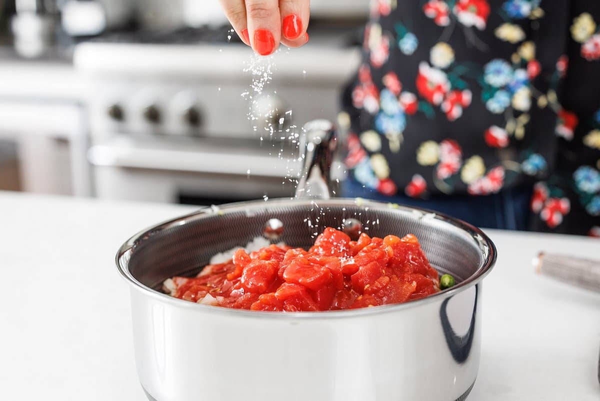 Seasoning green beans and tomatoes in pot with salt.
