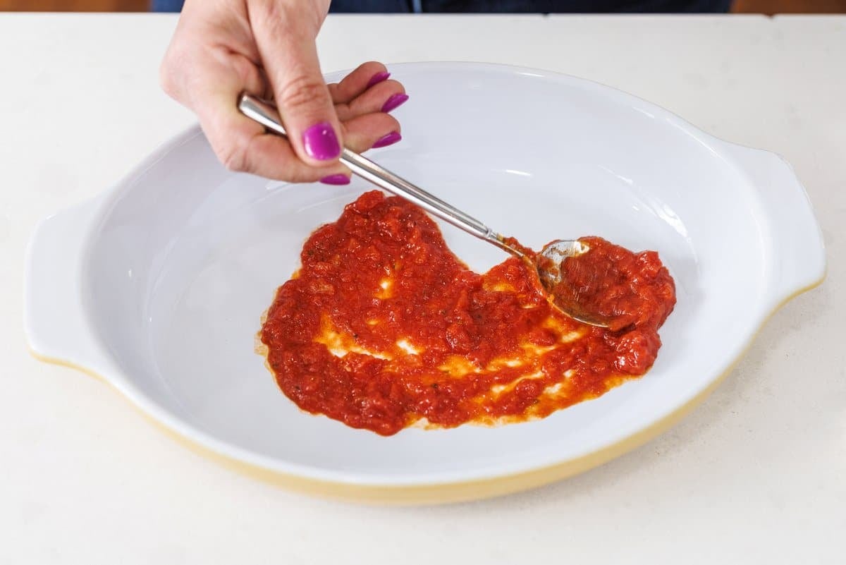 Spreading tomato sauce in the bottom of a baking dish with a spoon.