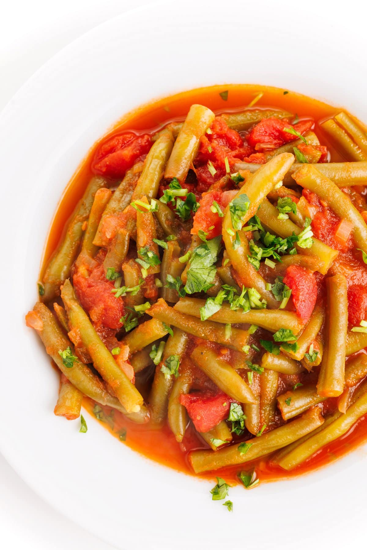 Top down view of a plate of stewed green beans garnished with fresh parsley.