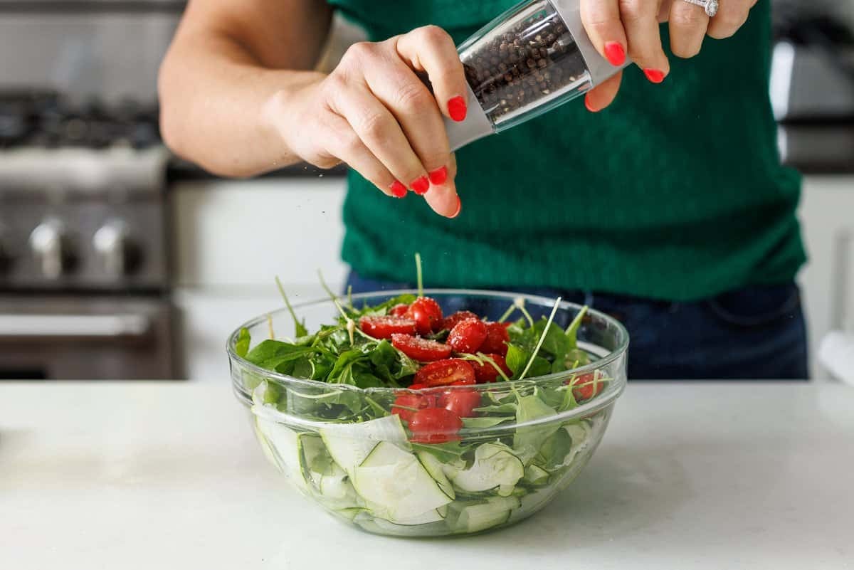 Seasoning cucumber zucchini salad with freshly ground pepper.