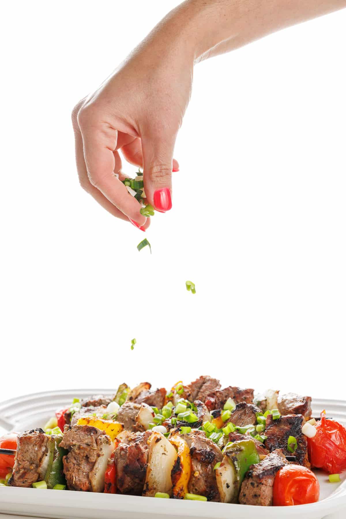 Garnishing Greek souvlaki beef kabobs with green onions.