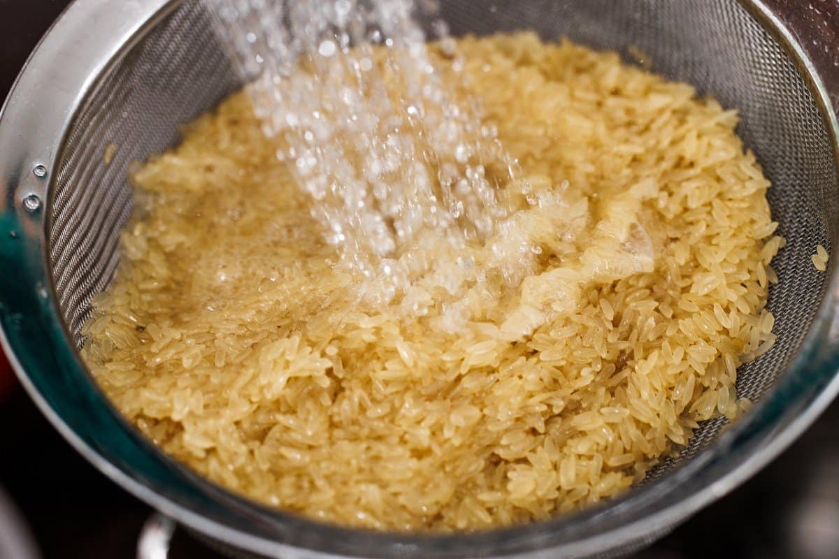 Rinsing white rice in a metal strainer.