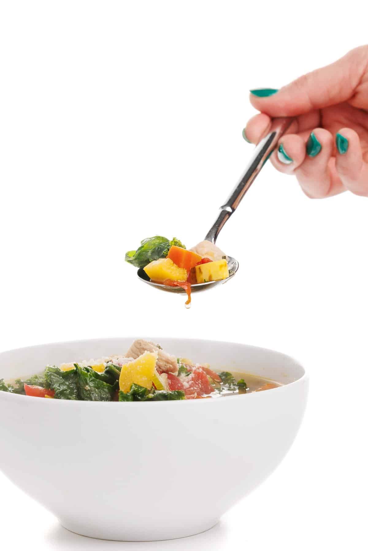 Spoonful of chicken soup with delicata squash and kale.