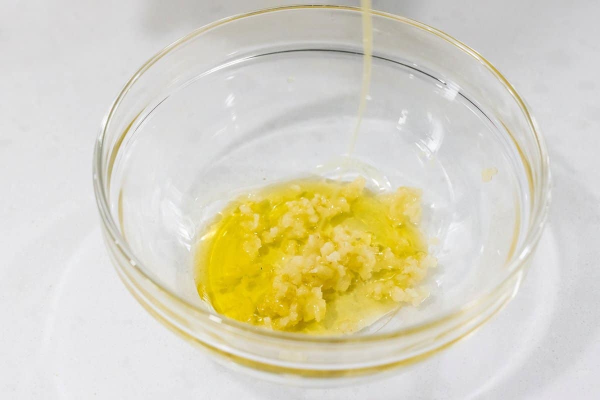 Drizzling olive oil into a bowl with minced garlic.