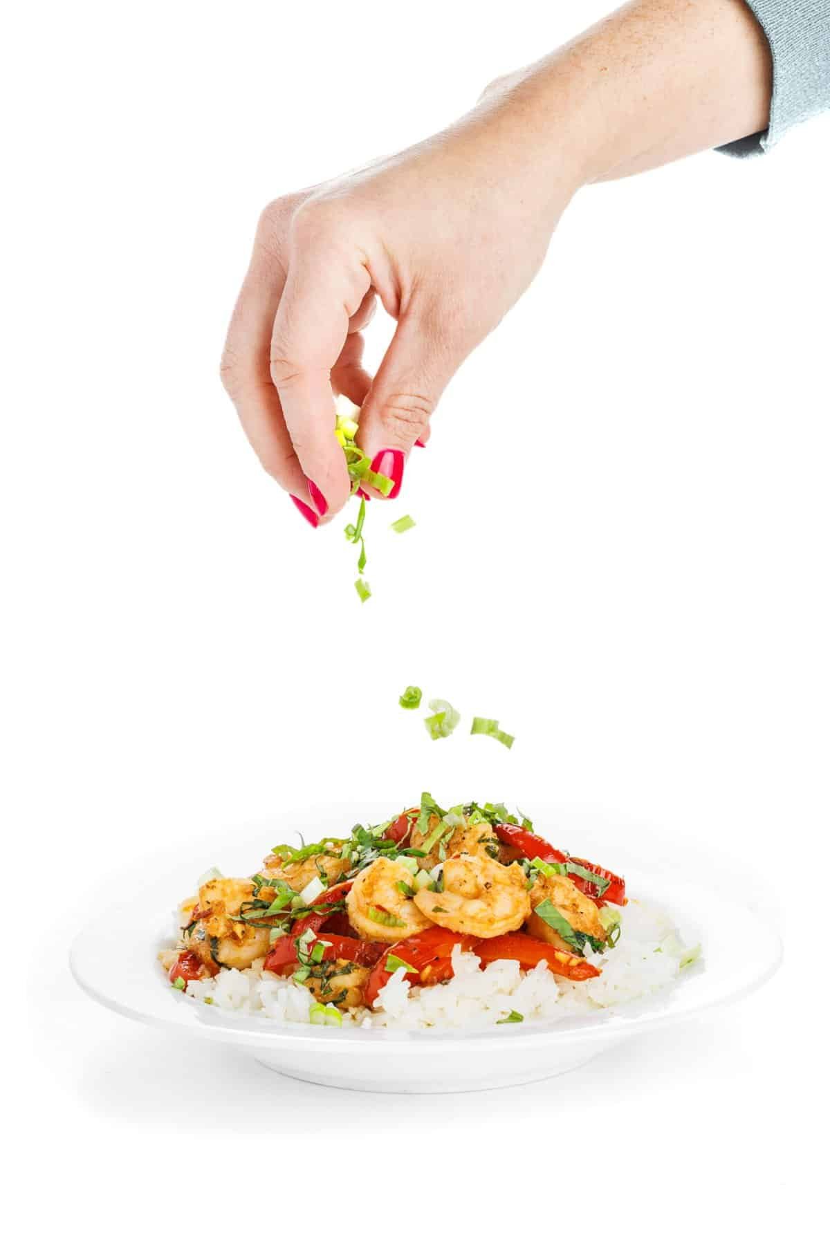 Garnishing thai basil shrimp with scallions.