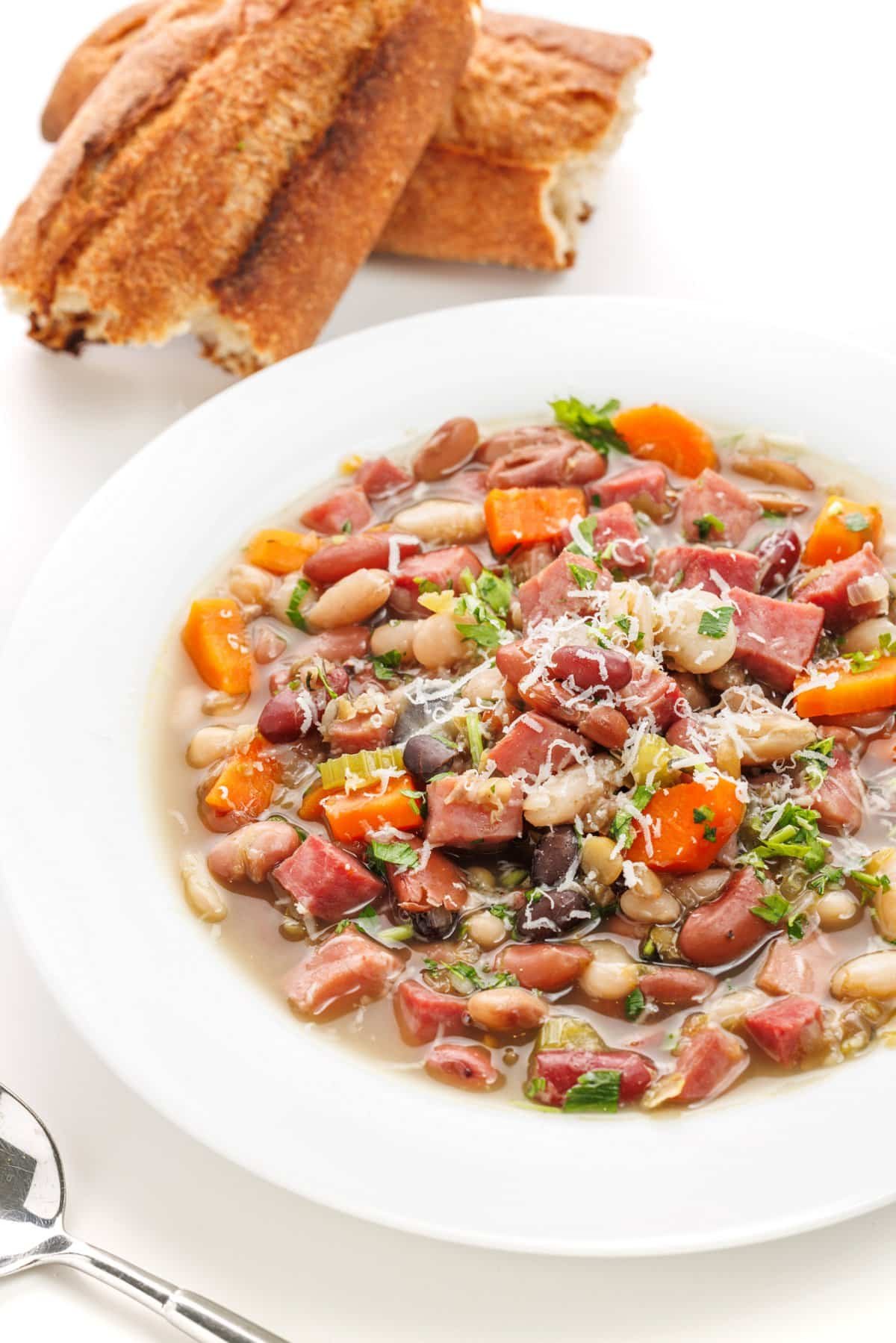 15 bean soup with ham in a white bowl garnished with parmesan cheese and fresh herbs.