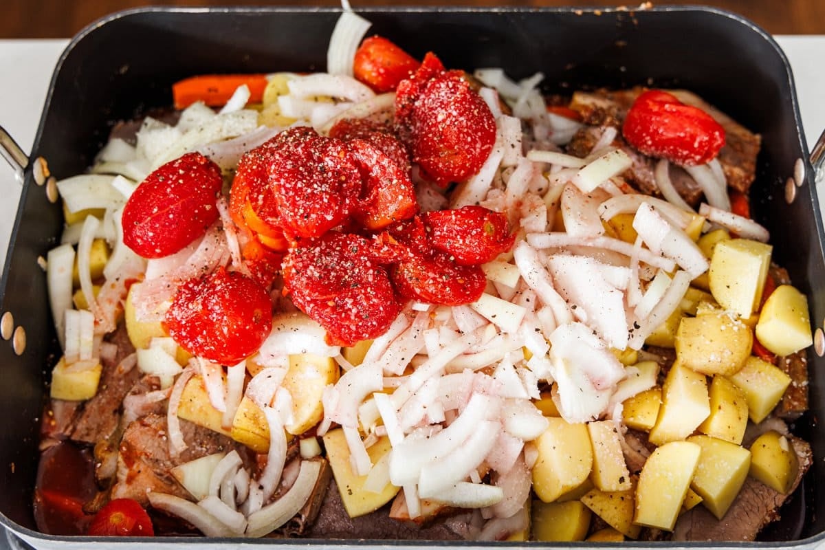 Brisket, potatoes, onion, and tomatoes added to roasting dish.