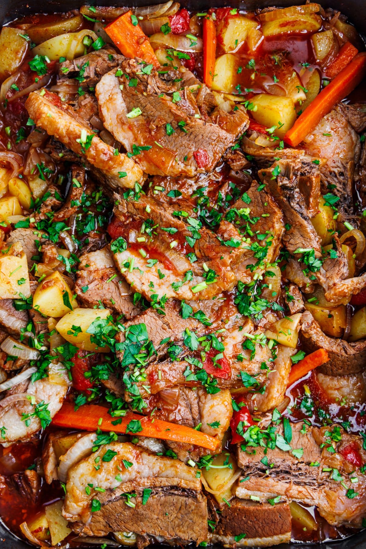 Cooked beef brisket with vegetables and garnished with fresh herbs.