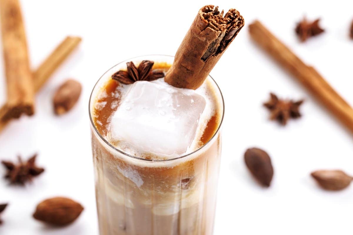 The top of a chai infused white Russian, with cloves and cinnamon sticks in the background.