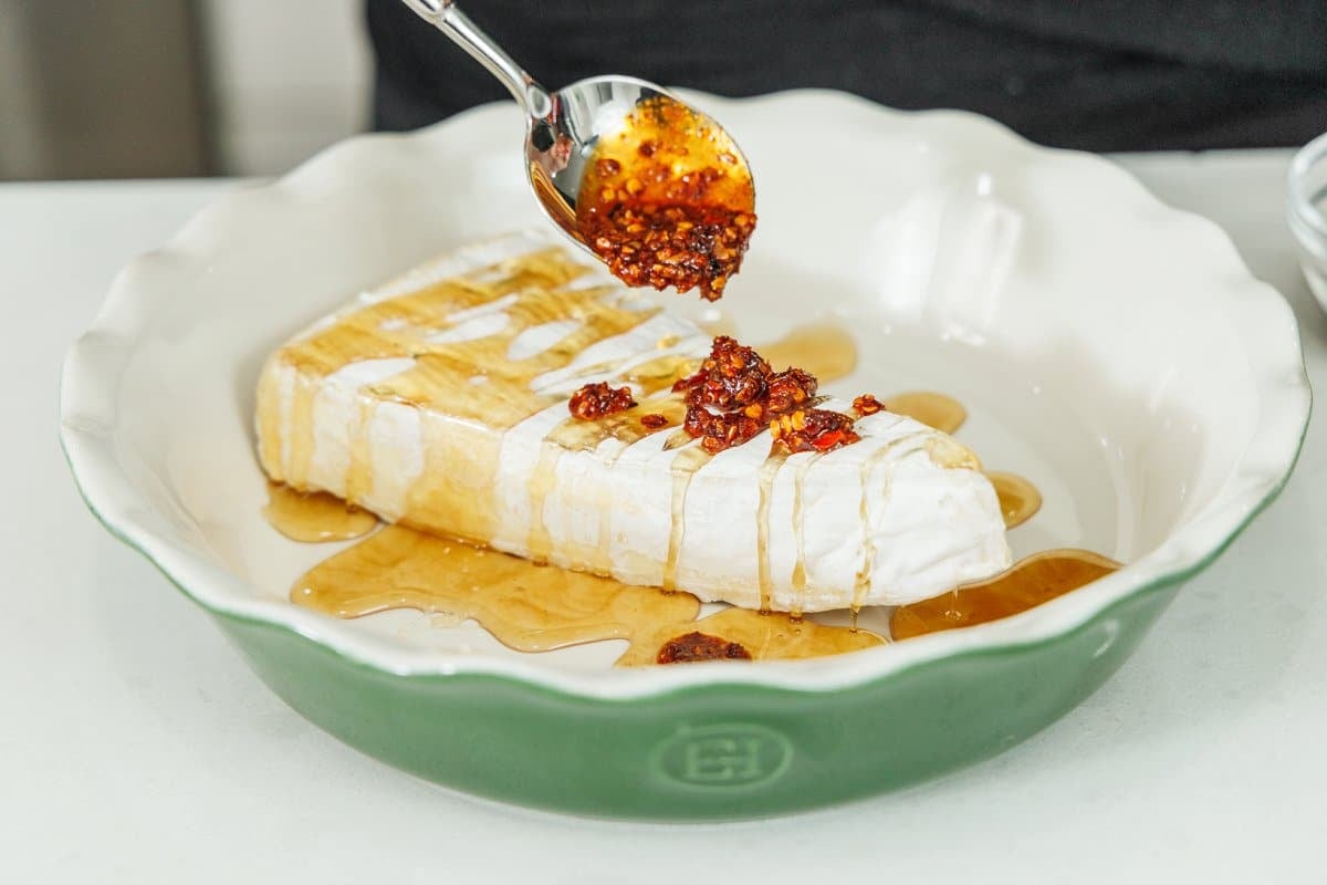 Adding chili crisp over top of honey drizzled brie wedge.