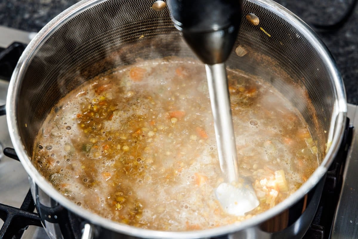 Using an immersion blender to blend arabic soup in a large metal pot.