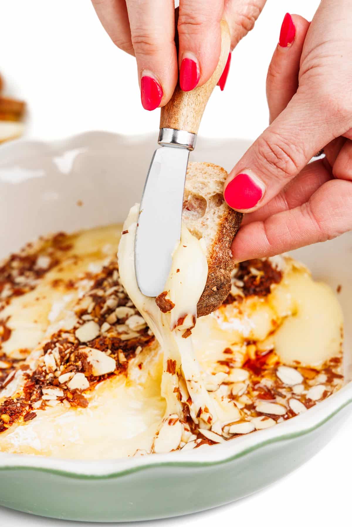 Spreading hot honey baked brie onto a slice of baguette.